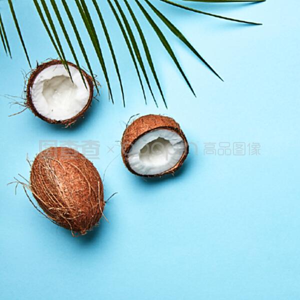 整個和一半的椰子,在藍色背景上的棕櫚葉和文本空間的副本。一個奇異的水果。扁平放。一個椰子和棕櫚綠葉在藍色背景上的副本空間。熱帶堅果。扁平放。